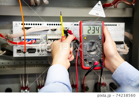 Electrician with multimeter in hands measures voltage in the electrical box. 74238560