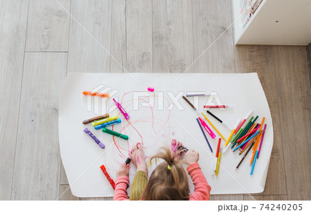 A little girl, sitting on the floor, enjoys creativity, drawing pictures with pencils on paper. top view A little girl, sitting on the floor, enjoys creativity, drawing pictures with pencils on paper. top view 74240205