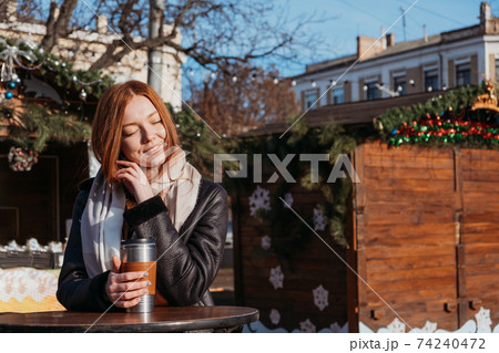 Slow living in city environment, Urban Slow life, mindfulness, enjoying the moment, work-life balance. Young redhead woman enjoying the sun and drinking take away coffee in winter city streets. Slow living in city environment, Urban Slow life, mindfulness, enjoying the moment, work-life balance. Young redhead woman enjoying the sun and drinking take away coffee in winter city streets. 74240472