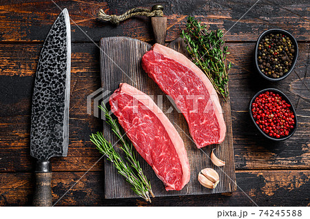 Raw top sirloin beef meat steak on a cutting wooden board. Dark wooden background. Top view Raw top sirloin beef meat steak on a cutting wooden board. Dark wooden background. Top view 74245588