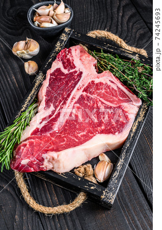 Porterhouse or T bone raw beef meat Steak with herbs and salt in wooden tray. Black wooden background. Top view 74245693