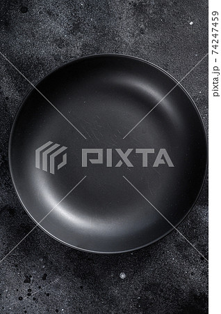 Black plate on textured black background. Top view. Copy space 74247459