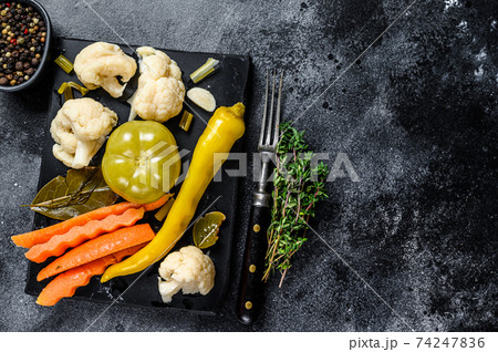 Fresh preserves vegetables, homemade delicious pickles on a marble board. Black background. Top view. Copy space Fresh preserves vegetables, homemade delicious pickles on a marble board. Black background. Top view. Copy space 74247836