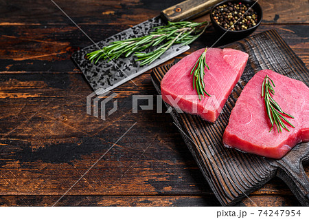 Raw tuna steaks on a wooden cutting Board with cleaver. Dark wooden background. Top view. Copy space 74247954