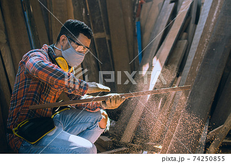 carpenter is working in a woodworking office.A white male carpenter is selecting the wood material and brushing off the sawdust. 74250855