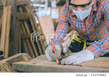 carpenter is working in a woodworking office.caucasion white Carpenter using tape measure to measure distance and marking with pencil 74250882