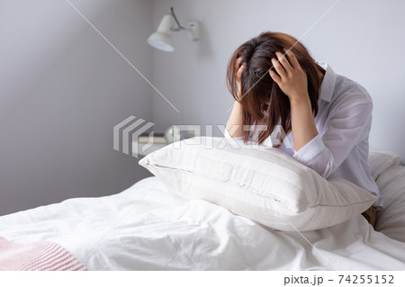 ベッドで女性が頭を抱えて悩んでいる　woman bed 74255152