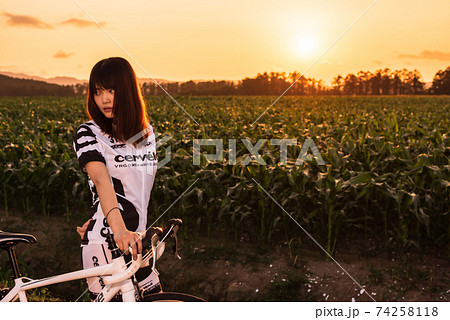 夕焼けに染まるサイクルウェアの女性ロードレーサー 74258118