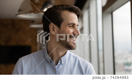 Optimistic young man looking at window thinking of good opportunities Optimistic young man looking at window thinking of good opportunities 74264983