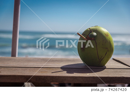 Coconut with a tube on the windowsill. Ocean view. Coconut water drink. Coconut with a tube on the windowsill. Ocean view. Coconut water drink. 74267420