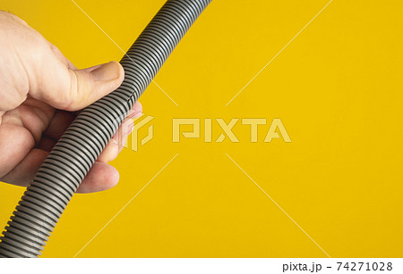 Against the yellow background the hands of a plumber are testing the integrity of a drain pipe: they highlight a crack that caused leaks and the replacement of the pipe. 74271028