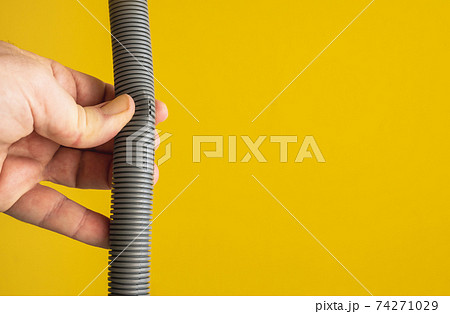 Against the yellow background the hands of a plumber are testing the integrity of a drain pipe: they highlight a crack that caused leaks and the replacement of the pipe. 74271029
