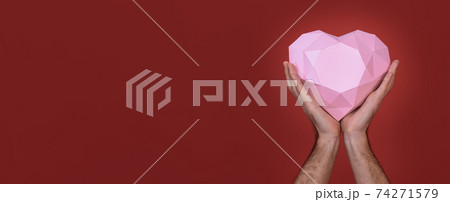 Polygonal pink heart in the hands of a man close-up. banner. On a red background. Greeting cards for Valentine's Day, weddings, declarations of love. Polygonal pink heart in the hands of a man close-up. banner. On a red background. Greeting cards for Valentine's Day, weddings, declarations of love. 74271579