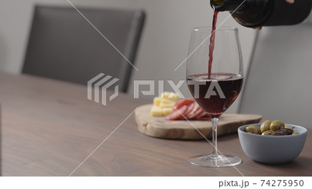pour red wine into wineglass with appetizers on background on wood table 74275950