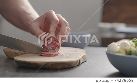 man slicing salame on olive wood board on concrete countertop man slicing salame on olive wood board on concrete countertop 74276058