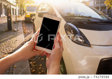 Hands with smartphone on a background of rental car at the charging station 74279589