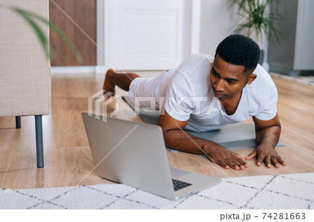 Close-up of strong African-American man exercising workout in horizontal plank position using laptop Close-up of strong African-American man exercising workout in horizontal plank position using laptop 74281663
