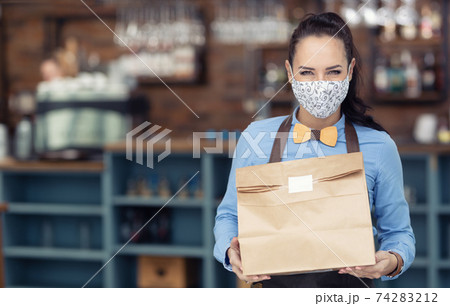 Face mask wearing restaurant employee hands over takeaway package during lockdown 74283212