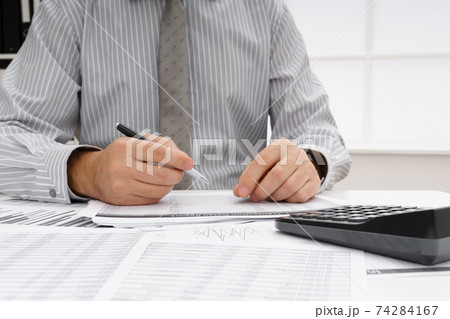 business concept - businessman's working table close view, checks financial reports, writes and counts business concept - businessman's working table close view, checks financial reports, writes and counts 74284167
