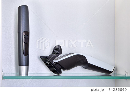 Rechargeable hairclipper is stored on shelf of your bathroom cabinet with cordless trimmer to remove hair from nose and ears. Rechargeable hairclipper is stored on shelf of your bathroom cabinet with cordless trimmer to remove hair from nose and ears. 74286849