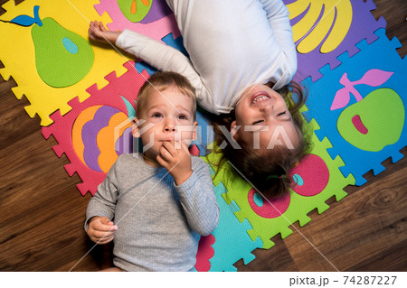 childhood, family friendship, games - close up portrait Two funny joy happy smiling little toddler peschool kids siblings twins brother with sister have fun lie playing on puzzles mat at home indoors 74287227