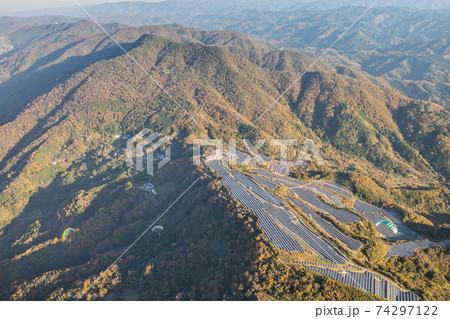 ソーラーパネルの傍を飛ぶパラグライダーと紅葉に染まる龍門山を空撮。和歌山県紀の川市 74297122