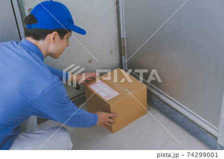玄関前に置き配をする配達員 74299001