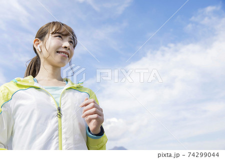 ワイヤレスイヤホンをしてランニングする若い女性   74299044