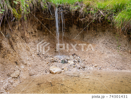 A washed out hole in the ground with a waterfall 74301431