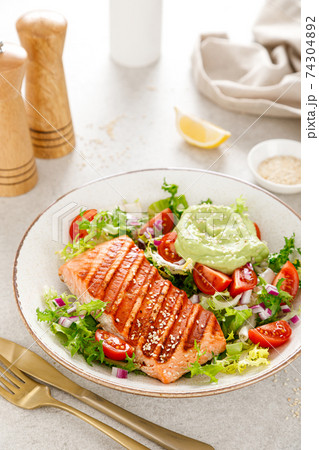 Grilled salmon fish fillet and fresh green lettuce vegetable tomato salad with avocado guacamole Grilled salmon fish fillet and fresh green lettuce vegetable tomato salad with avocado guacamole 74304892