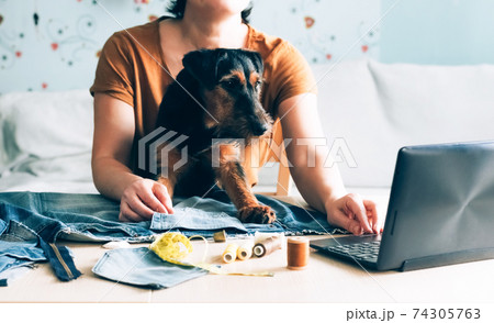 A woman with a pet in her arms is learning to watch sewing lessons online A woman with a pet in her arms is learning to watch sewing lessons online 74305763