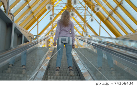 Young woman standing on the escalator Young woman standing on the escalator 74306434