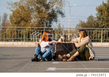 Young women with shopping bags sitting on parking Young women with shopping bags sitting on parking 74313971