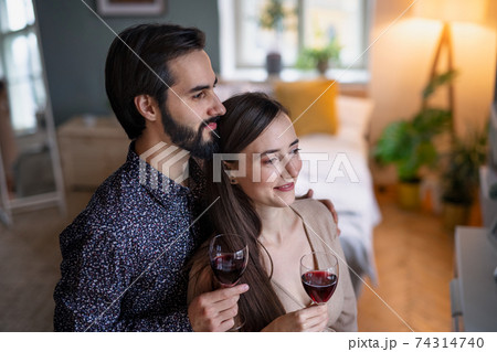 Young couple in love holding glasses of wine indoors at home. 74314740