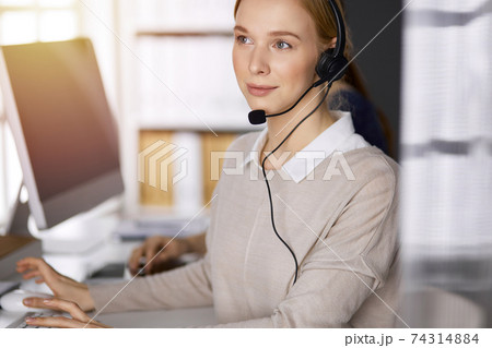 Businesswoman talking by headset while sitting in sunny office. Call center and diverse people group in business 74314884