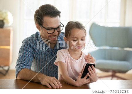 Happy dad and small daughter watch video on cellphone 74315258