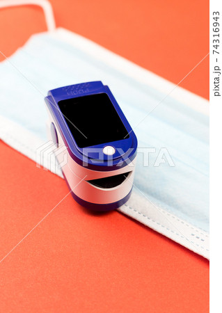 Pulse oximeter and protective medical mask on orange background 74316943