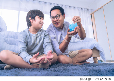 Father teaching son in money saving by inserting coin into a blue piggy bank for Financial concept. 74321910