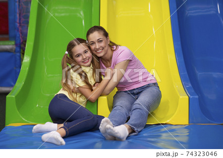 Portrait of happy mother and her teen daughter hugging near colorful slide at indoor entertainment centre for kids 74323046