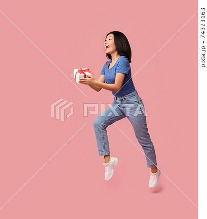 Jumping excited asian lady holding present box 74323163
