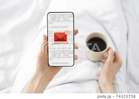 Woman Holding Phone With E-Mail Message Lying In Bed Indoor 74323758