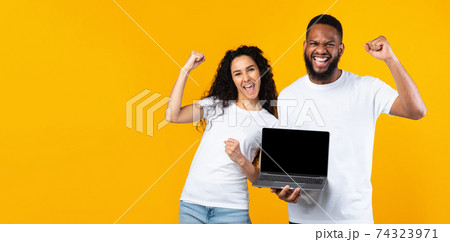 Multiracial Couple Showing Laptop Screen Gesturing Yes Over Yellow Background 74323971