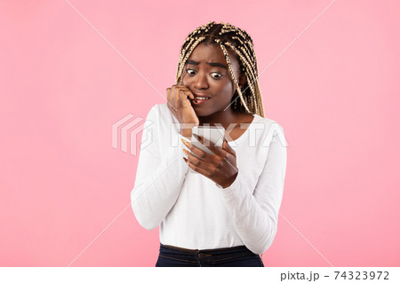 Anxious scared black woman looking at phone seeing bad news 74323972