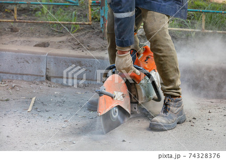 A worker uses a portable chainsaw and a diamond cutting disc to cut old asphalt on the road. 74328376