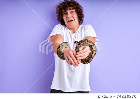 young caucasian male makes funny face grimace while holding snake in hands 74328870
