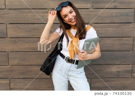 Photo of beautiful woman wearing white t-shirt holding computer laptop and black sunglasses staying 74330130
