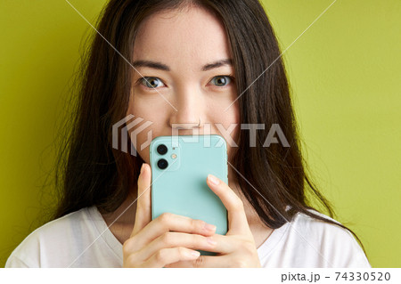 beautiful brunette woman hiding secret information, message in the smartphone isolated on green background 74330520
