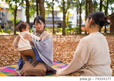 公園で赤ちゃんと抱っこしてママ友と話す女性 困る の写真素材