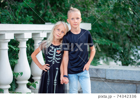 Modern children. Brother and sister in black robes stand by the handle. Skeleton pattern on dress 74342336