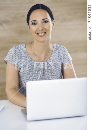 Cheerful smiling businesswoman working with laptop computer while sitting at the desk in modern office. Middle aged female lawyer or auditor at work. Business people concept 74342655